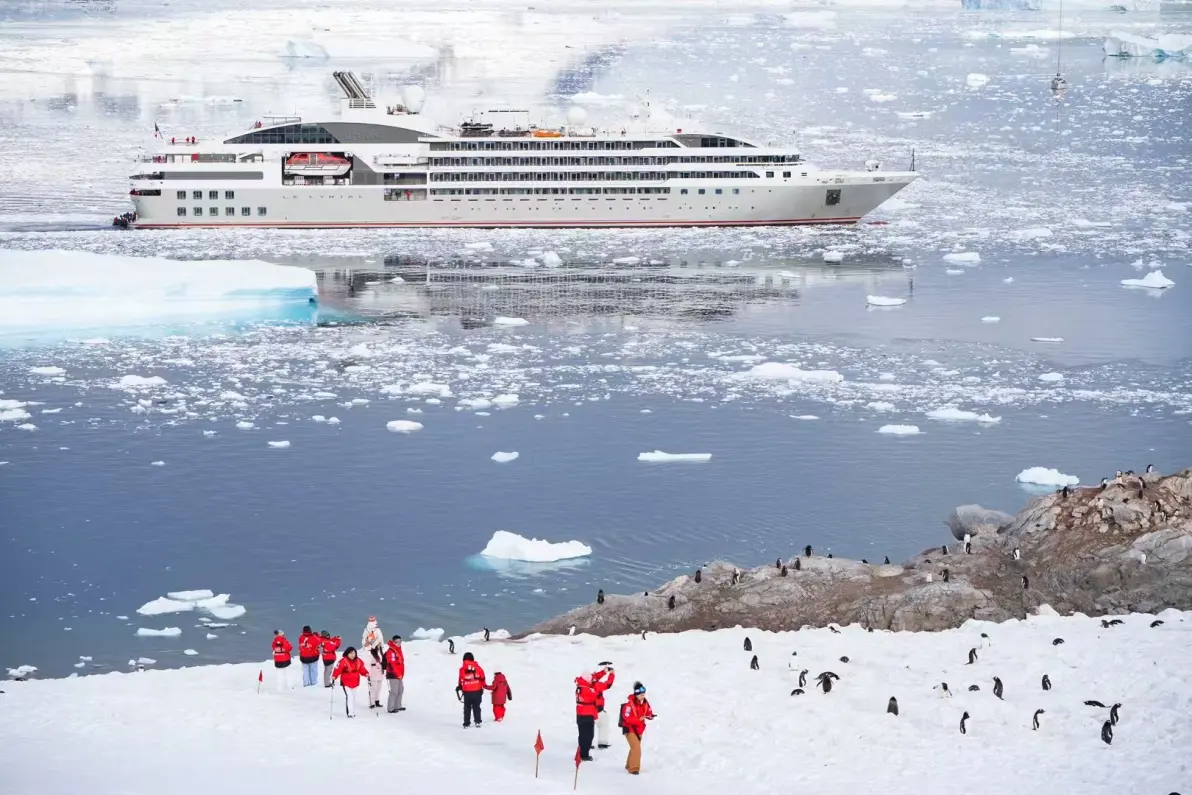 探险邮轮停在浮冰海面上,旅客在有企鹅的雪地上行走
