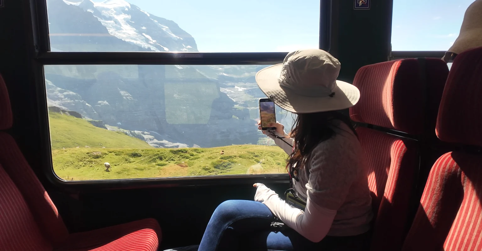 戴帽子的旅客坐在观光车窗边，窗外是山谷和雪山